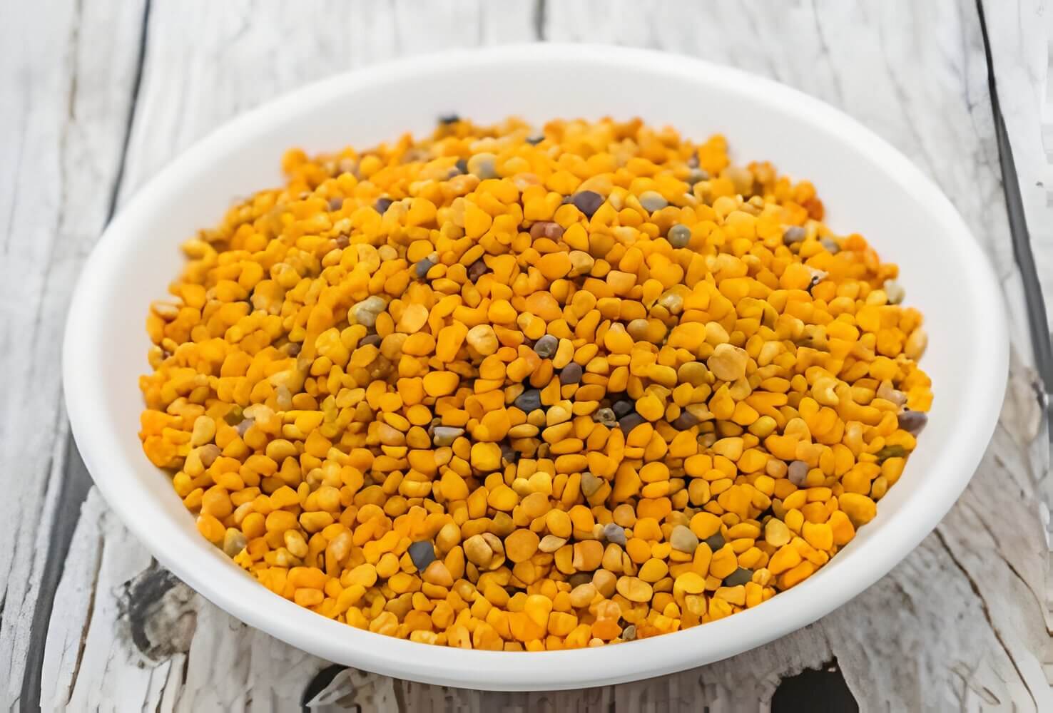 Bowl of bee pollen granules on a wooden table.